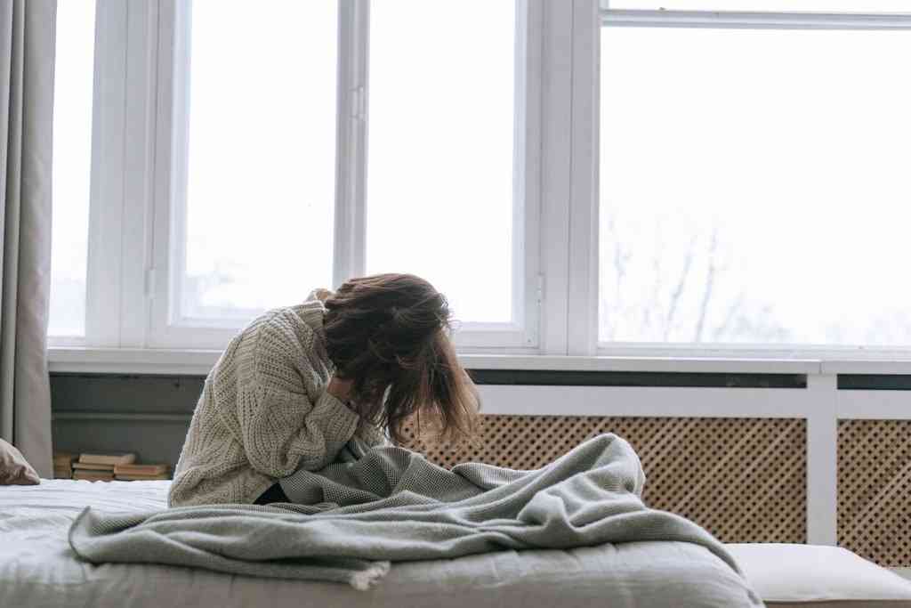 Девушка сидит в постели после просыпания на фоне окна